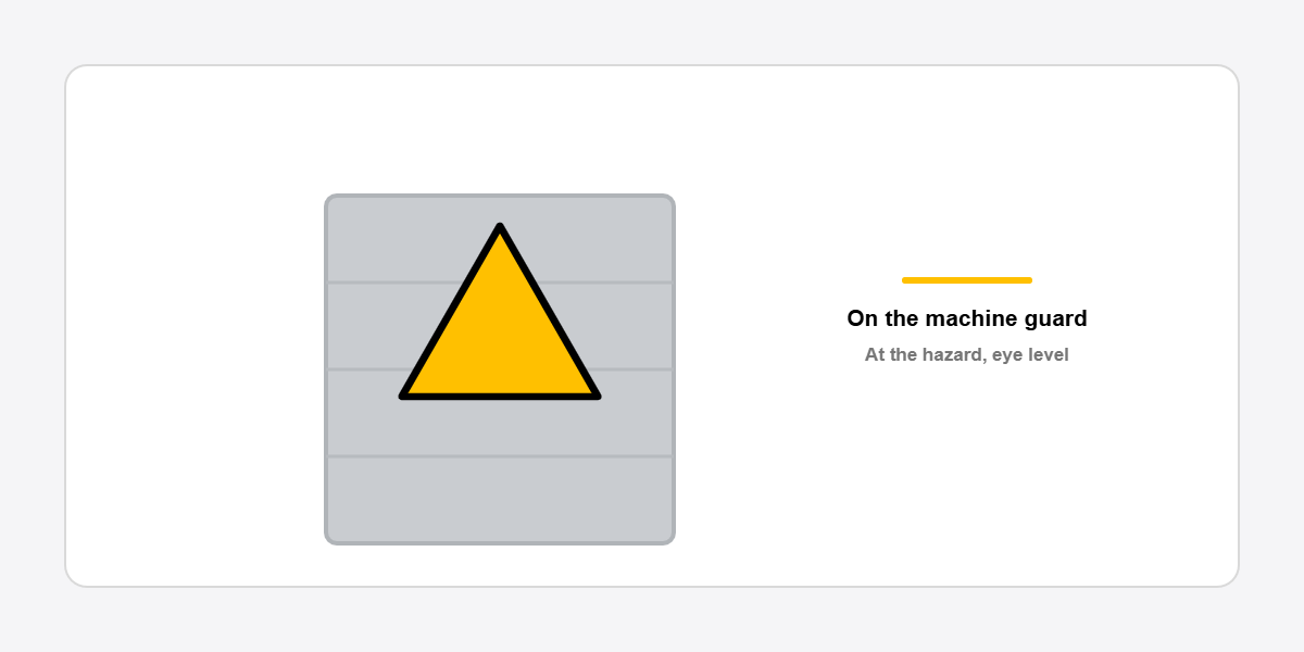 yellow triangular warning sign fitted on a machine guard in a workshop